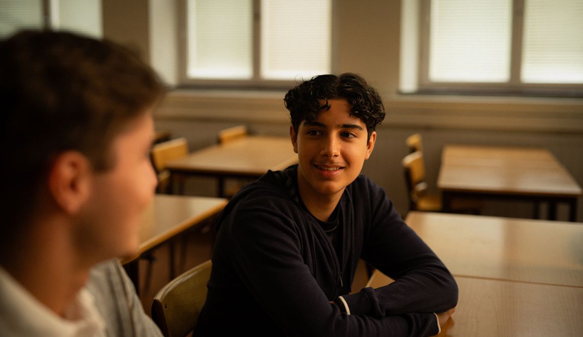 två ungdomar i ett klassrum sitter vid en skolbänk och pratar om självmord bland barn och unga