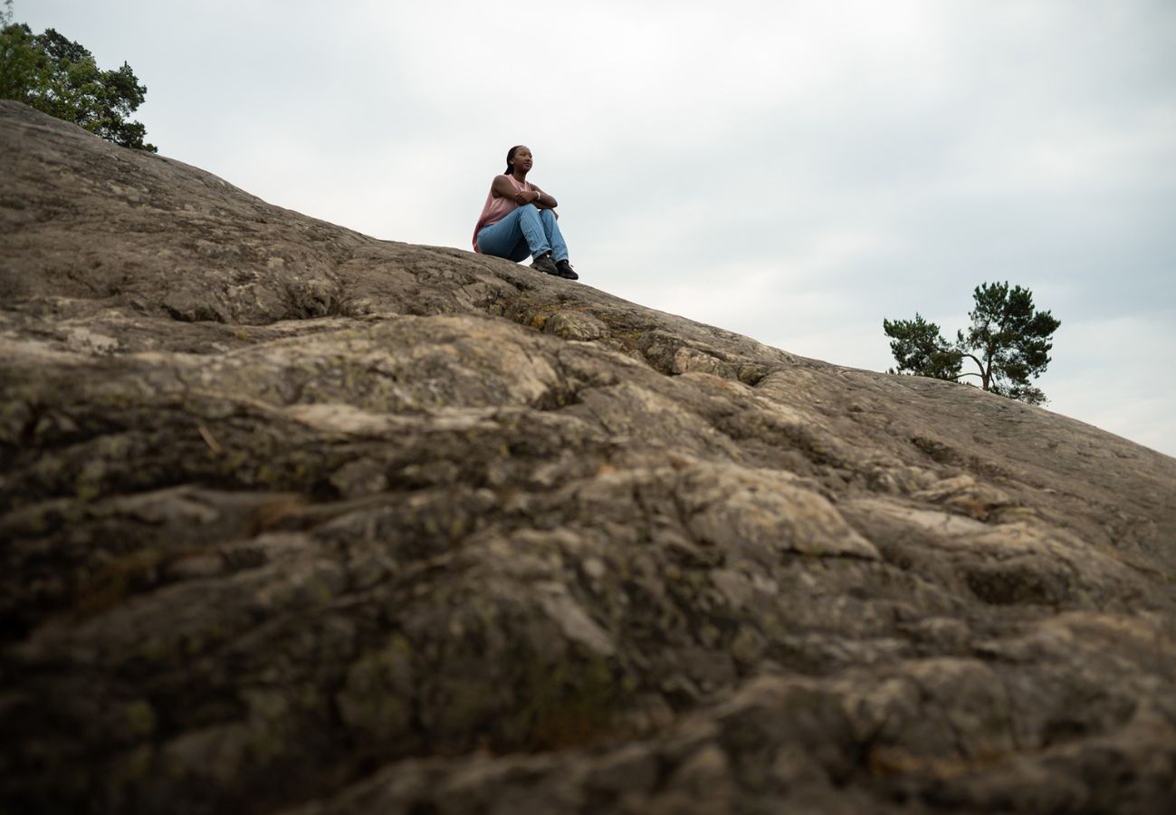 En ung flicka sitter ensam på ett berg och blickar ut.