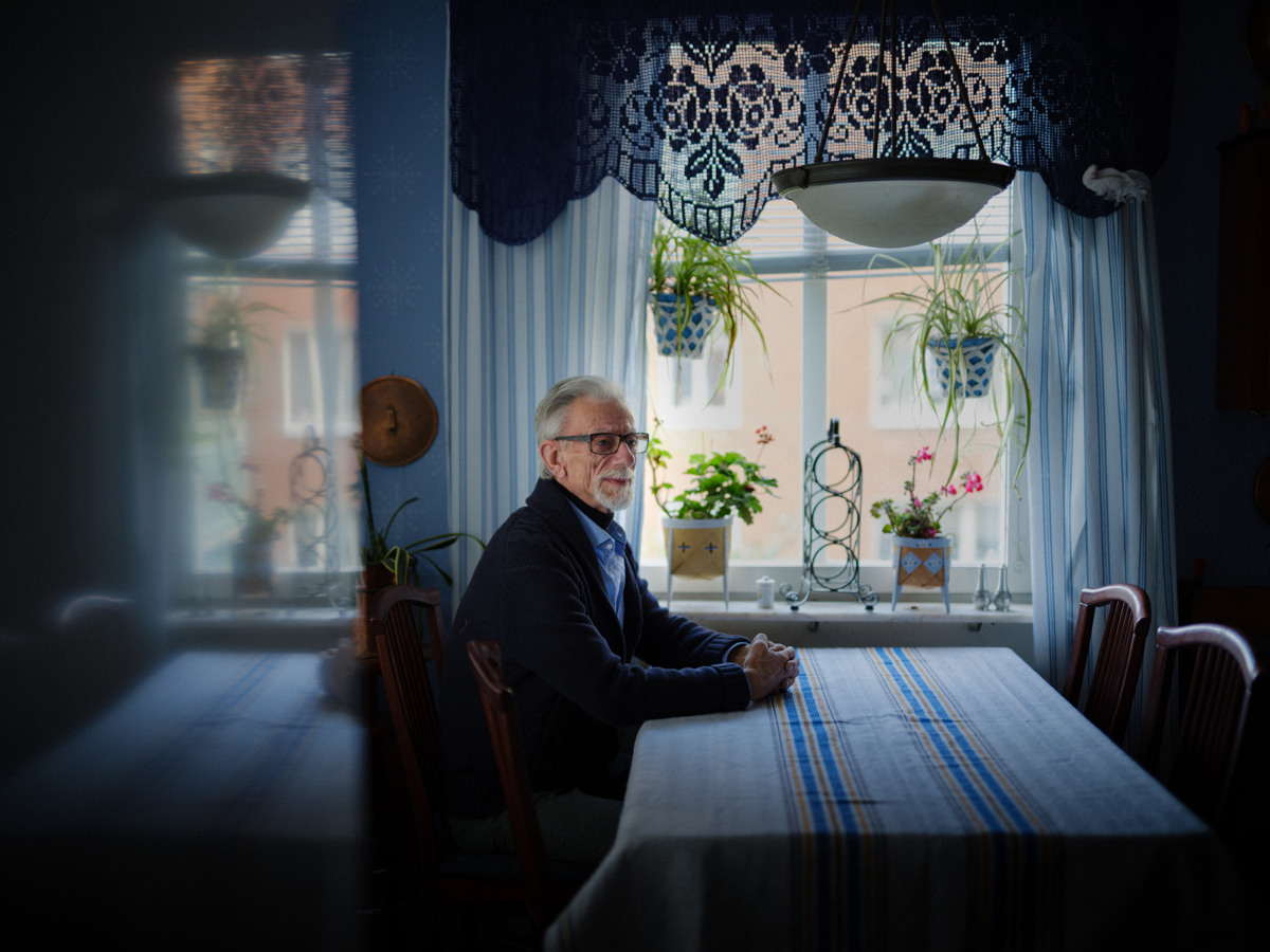 Äldre man sitter ensam vid ett bord framför ett fönster.